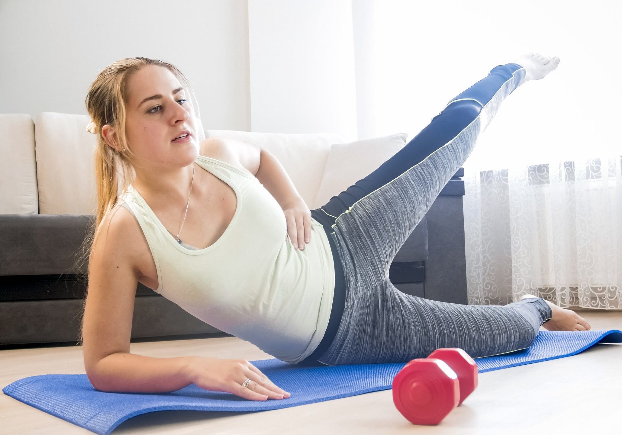 Young woman stretching legs on fitness mat at home